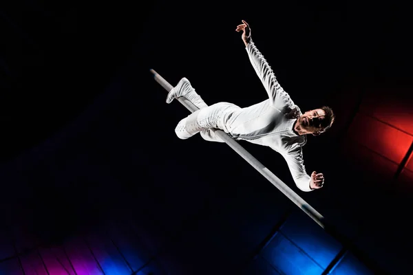 Low angle view of handsome acrobat holding metallic pole with legs while performing in circus — Stock Photo