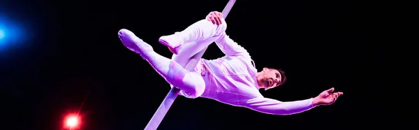 Panoramic shot of handsome acrobat holding metallic pole while performing in circus — Stock Photo