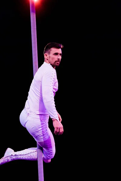 Back light near handsome acrobat looking away while performing on black — Stock Photo