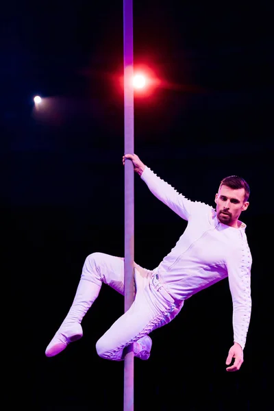 Acrobat mirando hacia otro lado mientras realiza en negro cerca de la luz de fondo - foto de stock