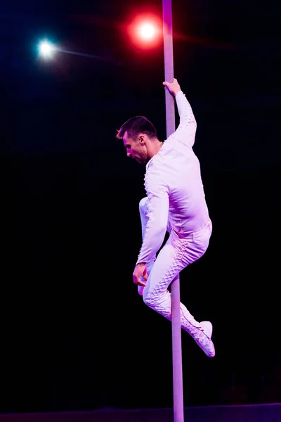 Acrobat holding pole while performing near red and blue back light on black — Stock Photo