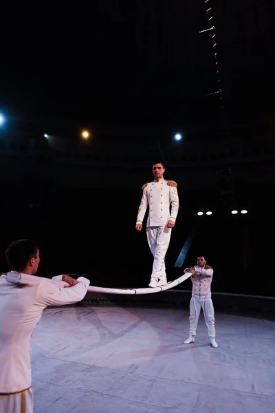 Acrobatas apoiando homem bonito andando sobre poste metálico no circo — Fotografia de Stock