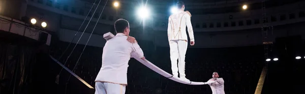 Panoramaaufnahme von Akrobaten, die Mann beim Gehen auf Metallstange im Zirkus unterstützen — Stockfoto