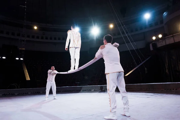 Acrobats supporting man walking on metallic pole in circus — Stock Photo