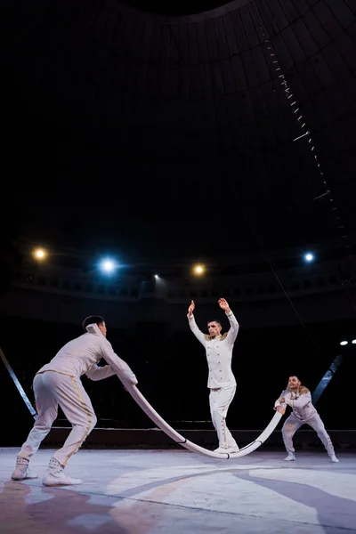 Acrobats supporting man with outstretched hands ready to jump on pole in circus — Stock Photo