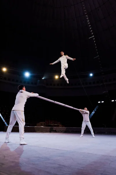 Acróbatas sosteniendo poste cerca de gimnasta saltando en circo - foto de stock