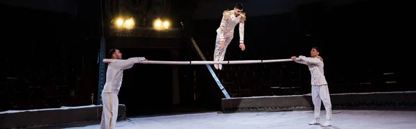 Panoramic shot of gymnast exercising on pole near acrobats in circus — Stock Photo
