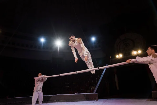 Красивый гимнаст, тренирующийся на шесте возле акробатов в цирке — стоковое фото