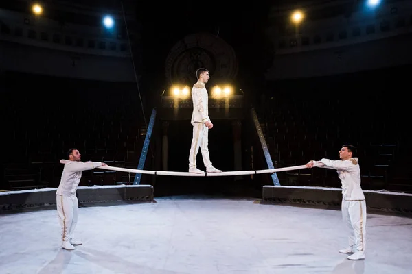 Вид сбоку гимнастки, занимающейся на шесте возле акробатов в цирке — стоковое фото