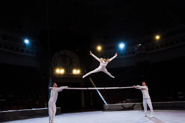 Gimnasta con las manos extendidas saltando en el poste cerca de acróbatas en circo - foto de stock