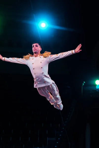 Handsome air acrobat with outstretched hands flying in arena of circus — Stock Photo