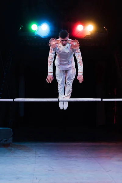Handsome gymnast in costume balancing near pole in arena of circus — Stock Photo