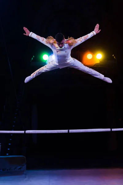 Handsome gymnast in costume jumping near pole in arena of circus — Stock Photo