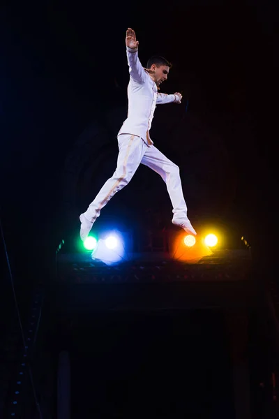 Vista lateral de gimnasta guapo con las manos extendidas saltando en la arena del circo — Stock Photo