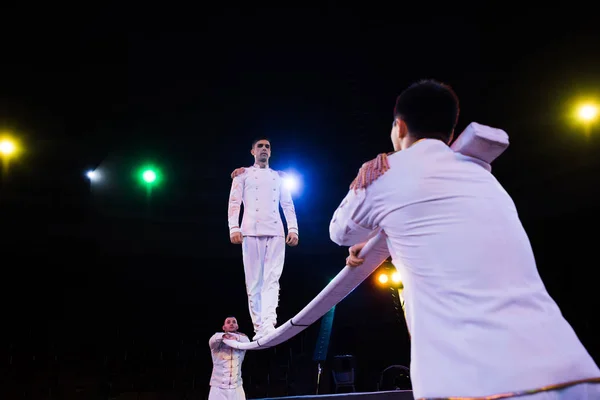 Low angle view of handsome air acrobat balancing on pole near men in circus — Stock Photo