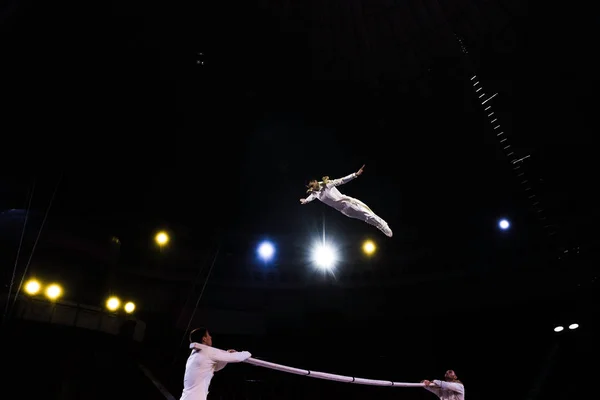 Acrobata de ar pulando enquanto se apresenta perto de homens no circo — Fotografia de Stock