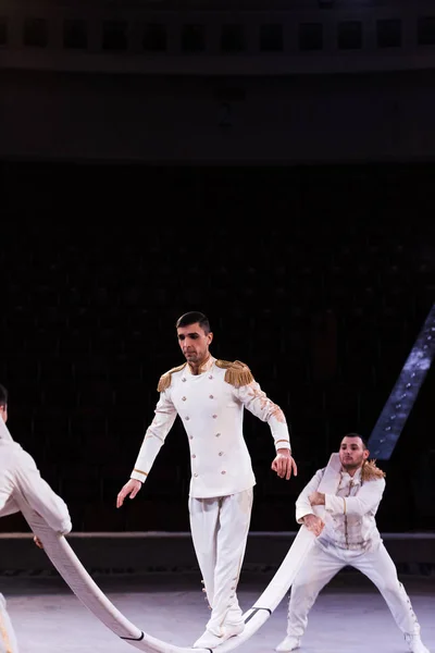 Acrobata de ar balanceamento no pólo metálico perto de homens no circo — Fotografia de Stock