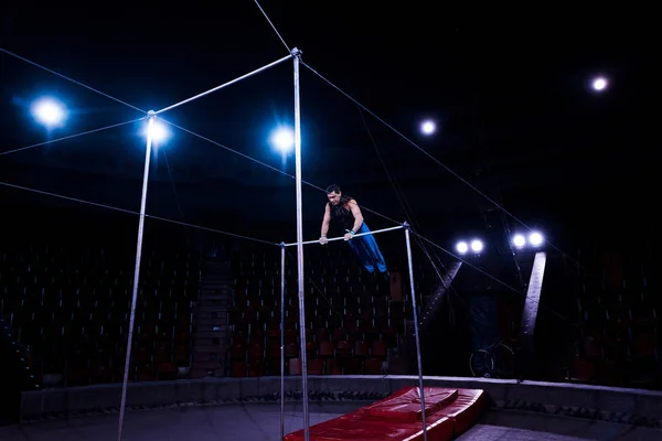 Handsome gymnast performing on horizontal bars in circus — Stock Photo