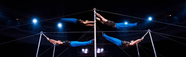 Panoramic shot of four gymnasts performing on horizontal bars in circus — Stock Photo