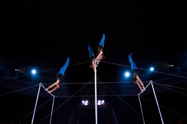 Gimnastas de bajo ángulo de visión que realizan en barras horizontales en la arena del circo - foto de stock