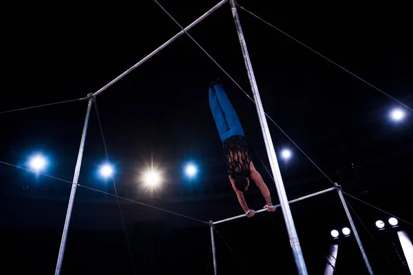 Back view gymnast performing on horizontal bars in circus — Stock Photo