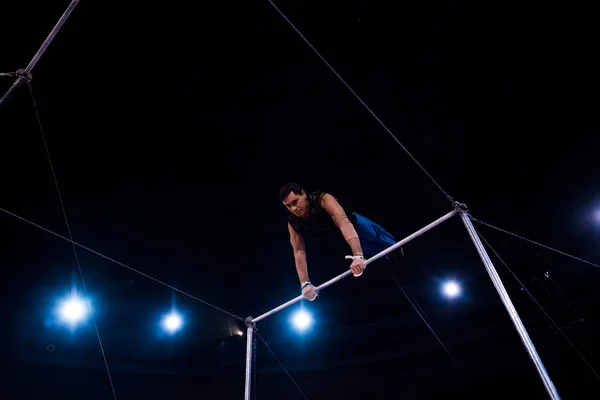 Blick aus dem tiefen Winkel auf einen hübschen Akrobat, der im Zirkus an horizontalen Stangen auftritt — Stockfoto