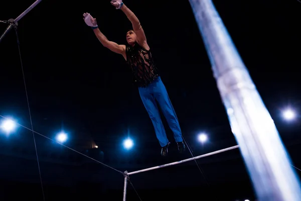 Selective focus of handsome gymnast performing on horizontal bars in circus — Stock Photo