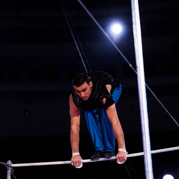 Athletic gymnast performing on horizontal bars in arena of circus — Stock Photo