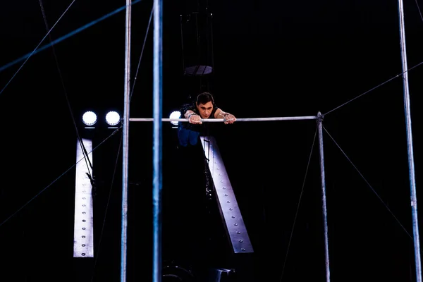 Athletic acrobat performing on horizontal bars in arena of circus — Stock Photo