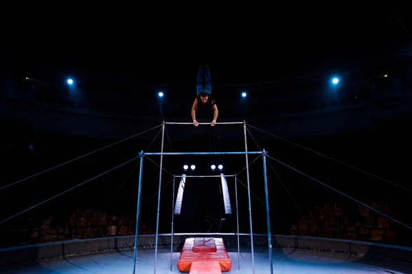 Красивый и атлетичный гимнаст, выступающий на горизонтальных брусьях на арене цирка — стоковое фото