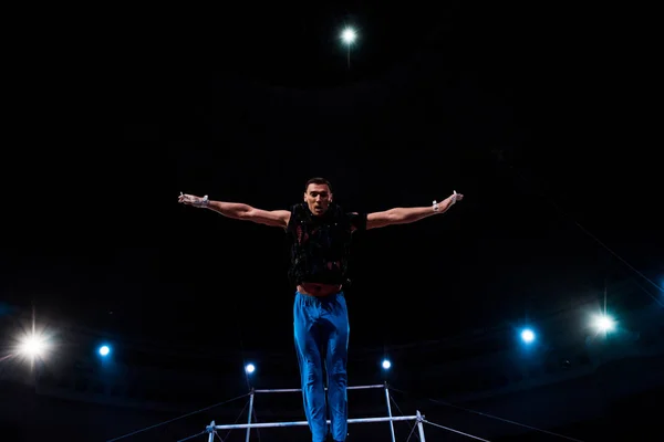 Athletic gymnast with outstretched hands performing near horizontal bars in arena of circus — Stock Photo