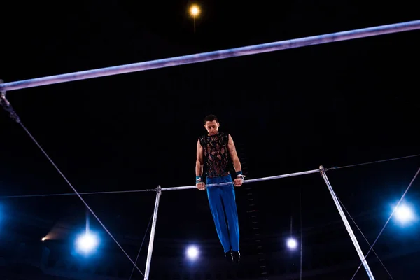 Low angle view of athletic gymnast performing on horizontal bars in arena of circus — Stock Photo