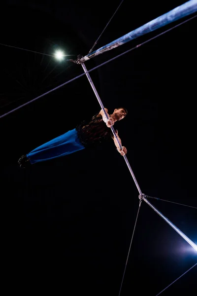 Bottom view of athletic gymnast performing on horizontal bars in arena of circus — Stock Photo