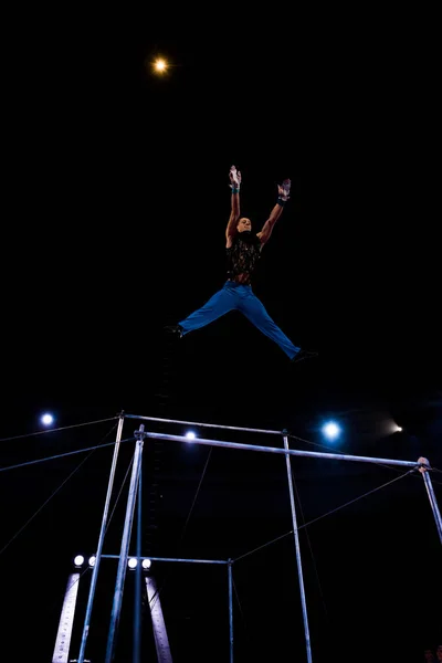 Низкий угол обзора прыжков гимнастки возле горизонтальных полос на арене цирка — стоковое фото