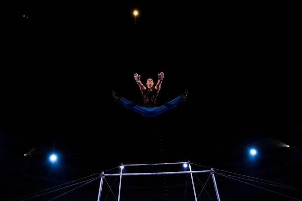 Low angle view of gymnast jumping near horizontal bars while performing in circus — Stock Photo