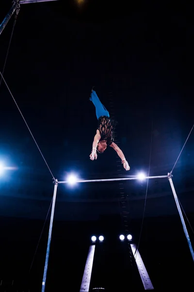 Низкоугловой вид гимнаста, балансирующего на горизонтальных перекладинах на арене цирка — стоковое фото