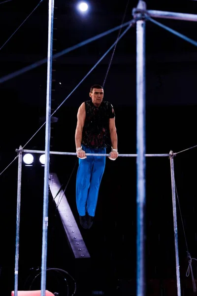 Selective focus of handsome and strong gymnast performing on horizontal bars in arena of circus — Stock Photo