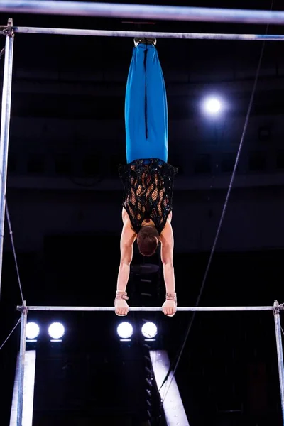 Задний вид сильного гимнаста, выступающего на горизонтальных брусьях на арене цирка — стоковое фото