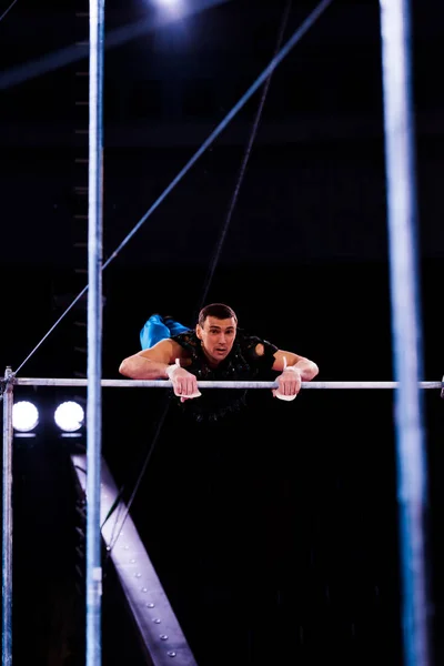 Selective focus of strong gymnast performing on horizontal bars in arena of circus — Stock Photo