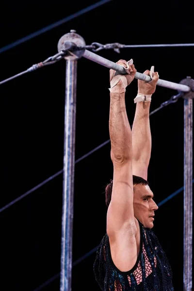 Vista laterale di ginnasta atletica che si esibisce su barre orizzontali in arena di circo — Foto stock