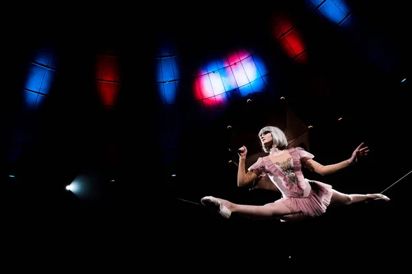 Low angle view of beautiful aerial acrobat holding umbrella and doing splits on rope — Stock Photo