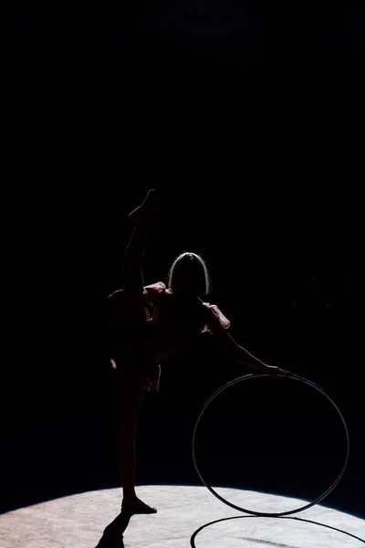Силуэт гибкого акробата, стоящего с обручем хулы на арене цирка — стоковое фото