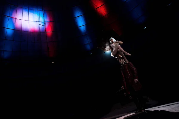 Attractive acrobat performing while sitting on hat of man in circus — Stock Photo