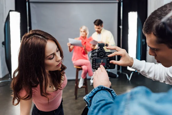 Selective focus of art director pointing with hand at display of digital camera near assistants — Stock Photo