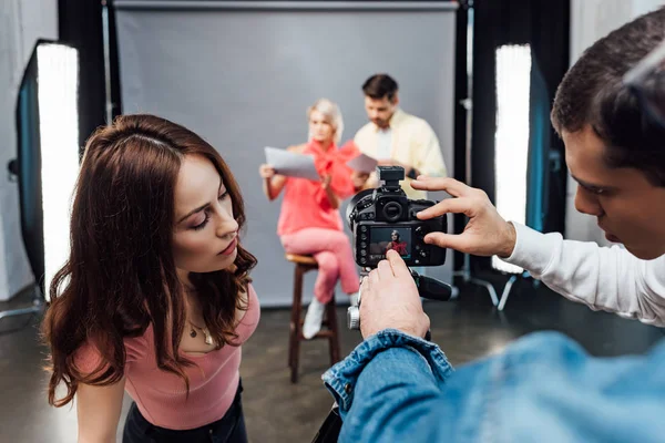 Foco seletivo do diretor de arte apontando com a mão na exposição da câmera digital perto de assistentes — Fotografia de Stock