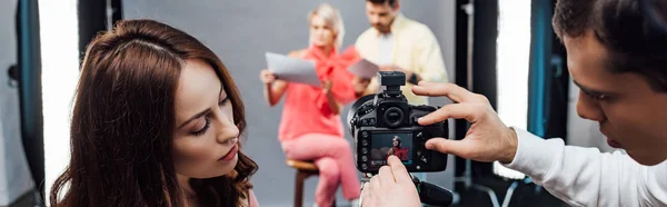 Panoramic shot of art director pointing with hand at display of digital camera near assistants — Stock Photo
