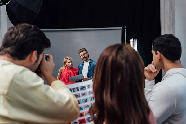 Enfoque selectivo de modelo atractivo cerca de director de arte barbudo en estudio fotográfico - foto de stock