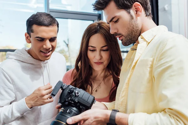 Attractive art director looking at digital camera near photographer and assistant — Stock Photo