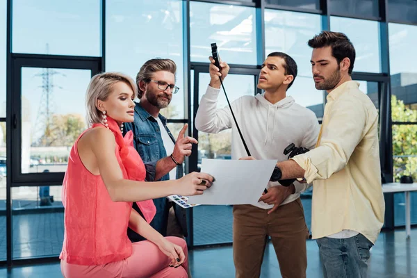 Attractive model and bearded art director looking at photo collage with assistants — Stock Photo