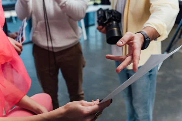 Visão recortada do fotógrafo apontando com o dedo para o papel perto de colegas de trabalho — Fotografia de Stock